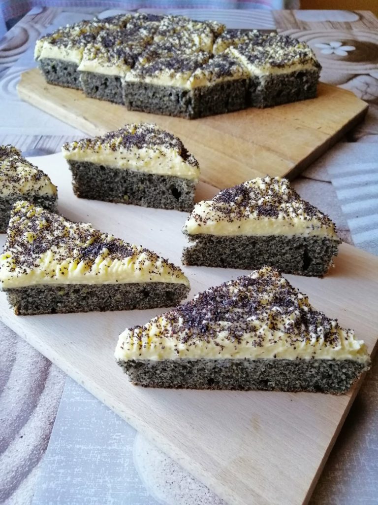 Mákos pudingos háromszög sütemény sárga vaníliakrémmel, mákkal megszórva, rusztikus tálaláson, szürke terítőn.